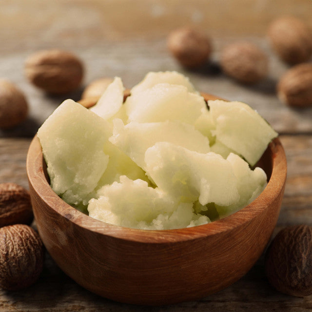 Wooden bowl filled with shea butter surrounded by nuts on a wooden surface