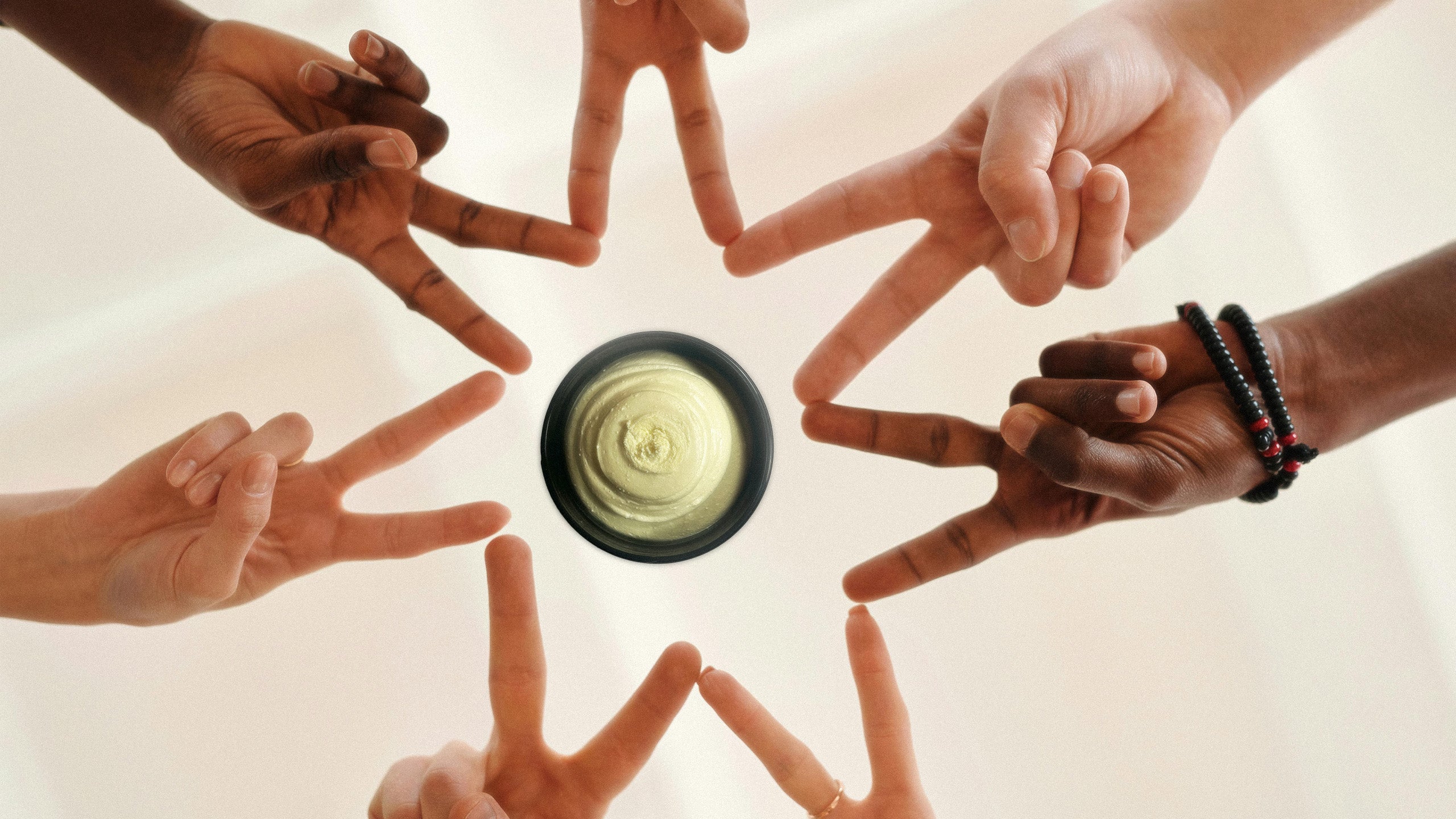 Hands forming a circle around a central Frog Guard Body Butter on a white background