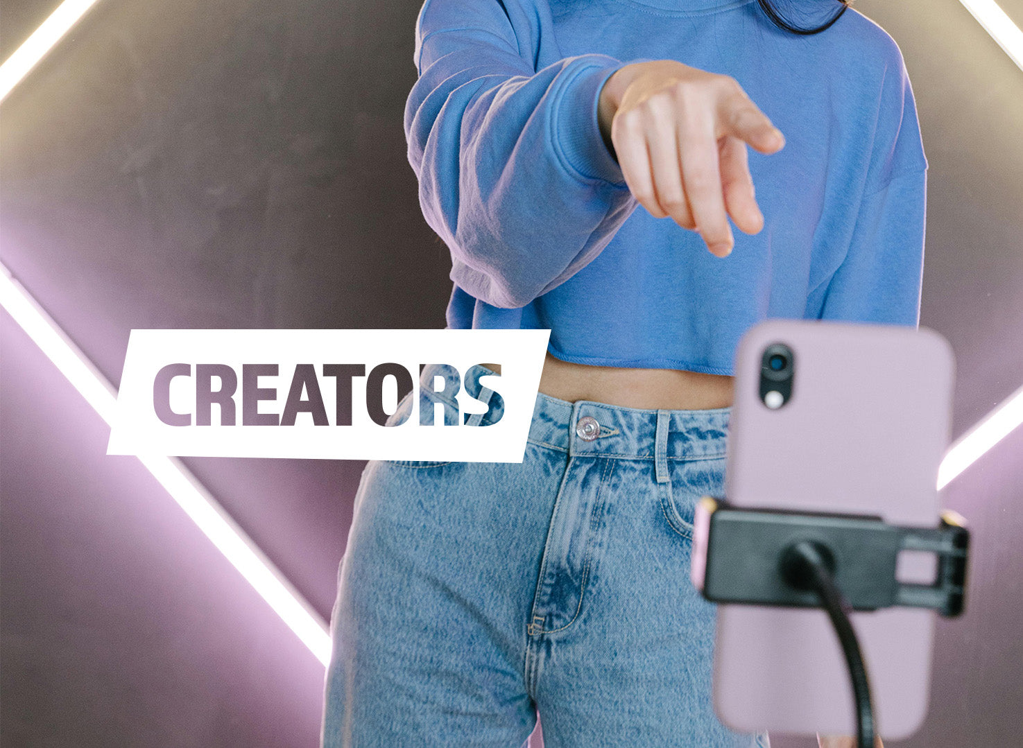 Person wearing a blue sweatshirt and jeans, holding a phone with 'CREATORS' text overlay.