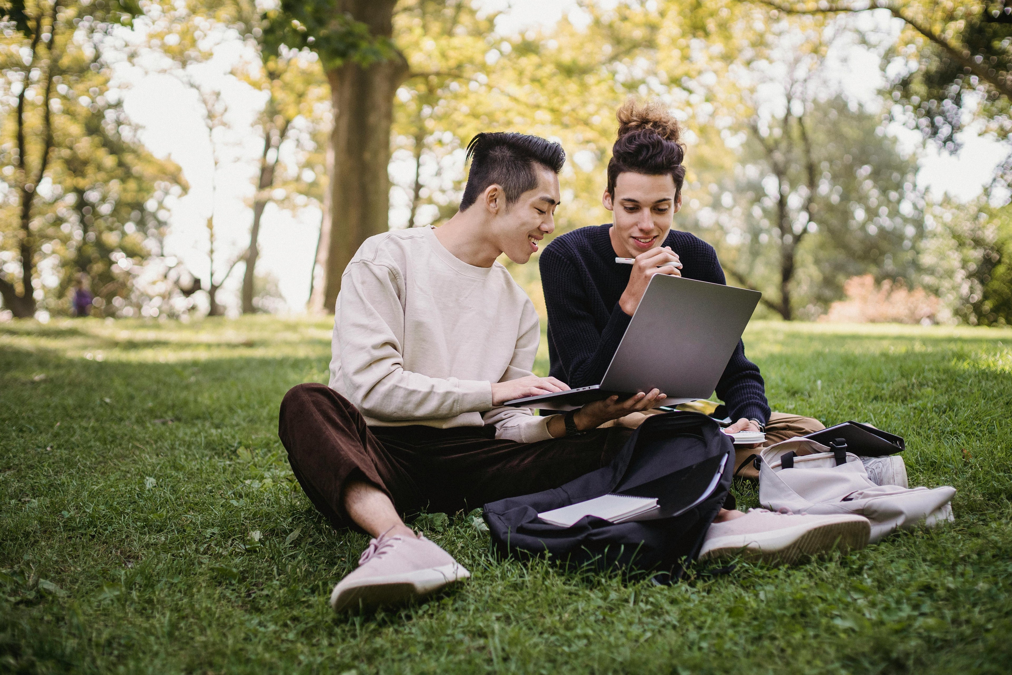 Two college students sitting on grass outdoors, looking at a laptop.