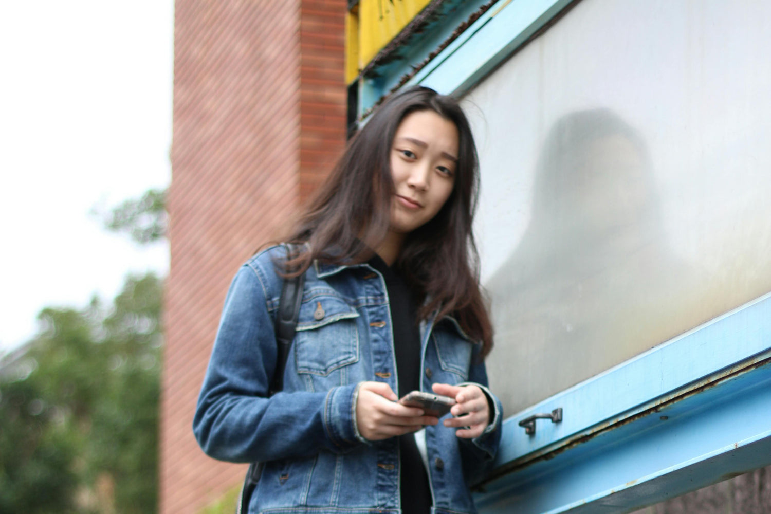 Woman in denim jacket using a phone outdoors with a building in the background